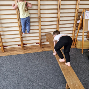 Chłopiec idzie na czworakach po ławeczce zawieszonej  skośnie