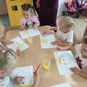 Dzieci malują żółtą farbą szablon uśmiechniętej buzi