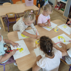 Dzieci malują żółtą farbą szablon uśmiechniętej buzi