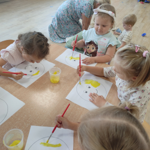 Dzieci malują żółtą farbą szablon uśmiechniętej buzi