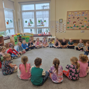 Dzieci siedzą w kole i śpiewają hymn przedszkolaków