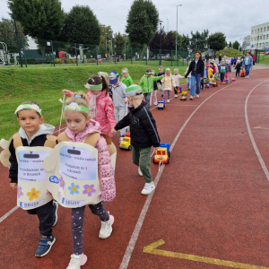 Dzieci z samochodami - zabawkami maszerują  po bieżni stadionu