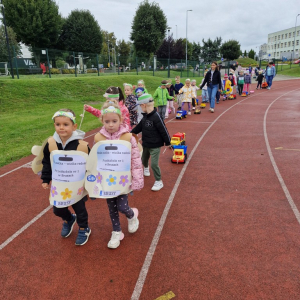 Dzieci z samochodami - zabawkami maszerują  po bieżni stadionu