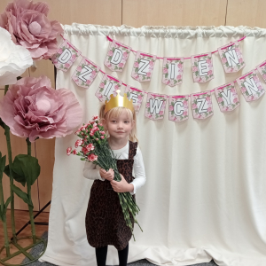 dziewczynka trzymająca kwiaty na tle napisu Dzień Dziewczynek