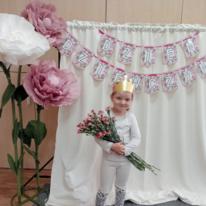 dziewczynka trzymająca kwiaty na tle napisu Dzień Dziewczynek