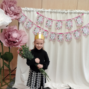 dziewczynka trzymająca kwiaty na tle napisu Dzień Dziewczynek