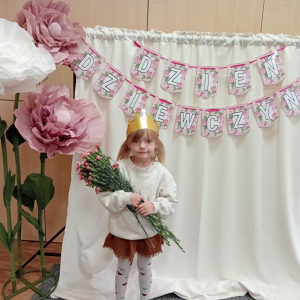 dziewczynka trzymająca kwiaty na tle napisu Dzień Dziewczynek