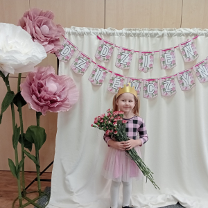 dziewczynka trzymająca kwiaty na tle napisu Dzień Dziewczynek