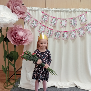 dziewczynka trzymająca kwiaty na tle napisu Dzień Dziewczynek