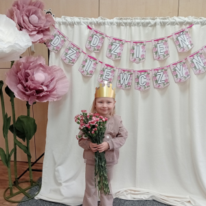 dziewczynka trzymająca kwiaty na tle napisu Dzień Dziewczynek