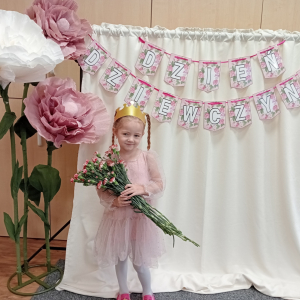 dziewczynka trzymająca kwiaty na tle napisu Dzień Dziewczynek