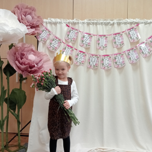 dziewczynka trzymająca kwiaty na tle napisu Dzień Dziewczynek