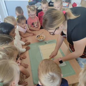 Dzieci obserwują nauczycielkę jak robić ciastka z jabłkami 