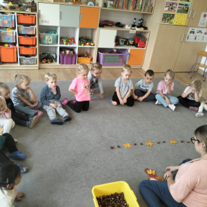 Dzieci siedzące w kole podczas zajęć i tworzące rytm z liści i kasztanów