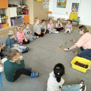 Dzieci siedzące w kole podczas zajęć i tworzące rytm z liści i kasztanów