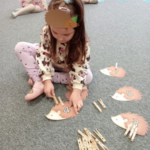 dziewczynka przyczepia klamerkowe kolce na ilustrację jeża