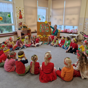 Dzieci słuchają piosenki o jabłku, śpiewnej przez Panią i ilustrowanej obrazkami