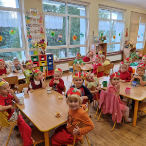 Dzieci siedząc przy stolikach, zjadają babeczki z jabłkami