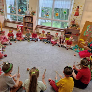 Dzieci rytmicznie uderzają pałeczkami   siebie, śpiewając piosenkę "Jabłko"