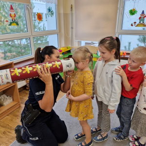 Dziewczynka patrzy  w tubę, aby zobaczyć   jak  wygląda w ciemności   człowiek w kamizelce  odblaskowej lub bez niej