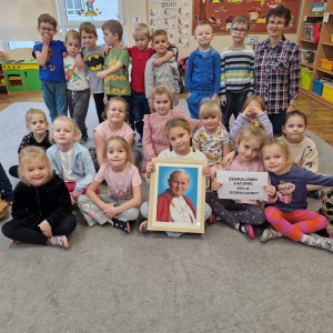 Dzieci z Panią Gabrysią (nauczycielką religii) trzymają obraz Jana Pawła II i kartkę z informacją o zebranej kwocie pieniężnej na Fundację Dzieło Nowego Dziesięciolecia