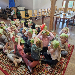 Dzieci siedząc na "latającym" dywanie zakładają "czapki"   z listków kapusty