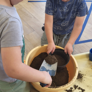 Chłopcy wsypują ziemię do doniczki.