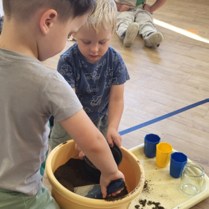 Chłopcy wsypują ziemię do doniczki.