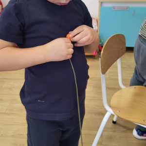 Chłopiec nawlekający koraliki na sznurek.