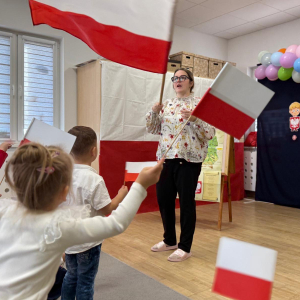 Nauczycielka i dzieci machające flagami Polski