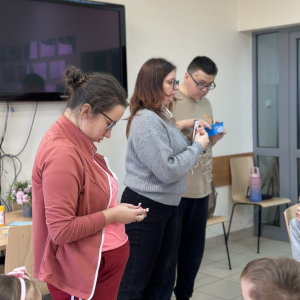 Pomoc i tłumaczenie: „Instruktor WTZ tłumaczy kolejne etapy tworzenia kartki, a dzieci chętnie słuchają i próbują samodzielnie.”