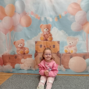 dziewczynka pozująca do zdjęcia na ściance tematycznej z okazji Dnia Pluszowego Misia