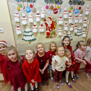 Dziewczynki na tle gazetki z pracami plastycznymi przedstawiającymi Mikołaje