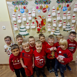 Chłopcy na tle gazetki z pracami plastycznymi przedstawiającymi Mikołaje