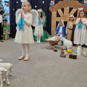 Dziewczynka w roli aniołka zapowiada dzieci zmierzające do  stajenki