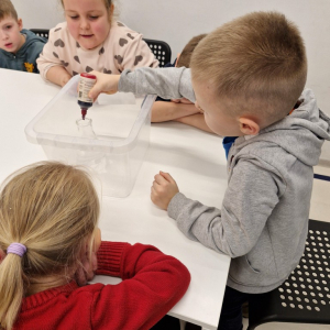 Chłopiec  zakrapla kilka kropli barwnika do kolby stożkowej 