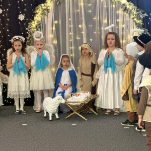 Pastuszkowie stoją przy żłóbku  z darami dla  Dzieciątka Jezus