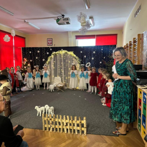 Pani Marysia zaprasza gości na przedstawienie jasełkowe "Betlejemscy wędrownicy"