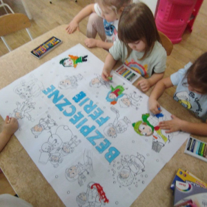 Dzieci kolorują plakat Bezpieczne ferie zimowe.