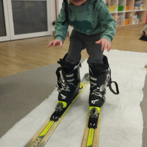 Dziecko przymierza strój i sprzęt narciarski.