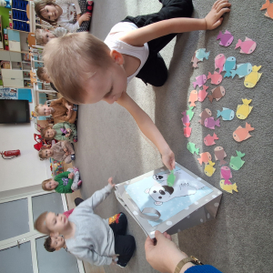 Dziecko wrzuca papierowe rybki ,karmi misia polarnego