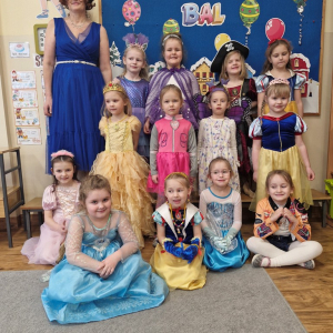 Dziewczynki w strojach karnawałowych z wychowawczynią na tle dekoracji karnawałowej