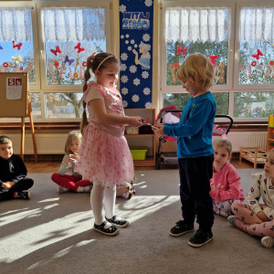 Chłopiec wręcza dziewczynce drewniany kwiatek z lizakiem z okazji Dnia Kobiet