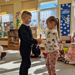 Chłopiec wręcza dziewczynce drewniany kwiatek z lizakiem z okazji Dnia Kobiet