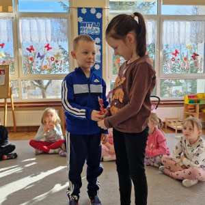 Chłopiec wręcza dziewczynce drewniany kwiatek z lizakiem z okazji Dnia Kobiet