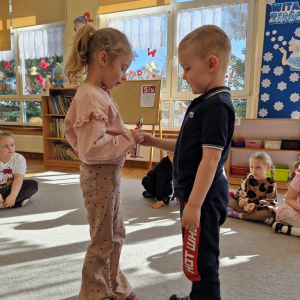 Chłopiec wręcza dziewczynce drewniany kwiatek z lizakiem z okazji Dnia Kobiet