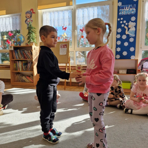 Chłopiec wręcza dziewczynce drewniany kwiatek z lizakiem z okazji Dnia Kobiet