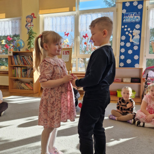 Chłopiec wręcza dziewczynce drewniany kwiatek z lizakiem z okazji Dnia Kobiet