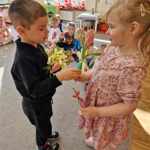 Chłopiec składa życzenia koleżance z grupy i wręcza tulipana z okazji Dnia Kobiet