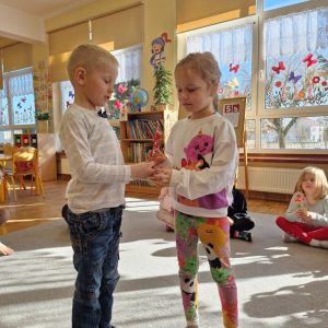 Chłopiec wręcza dziewczynce drewniany kwiatek z lizakiem z okazji Dnia Kobiet